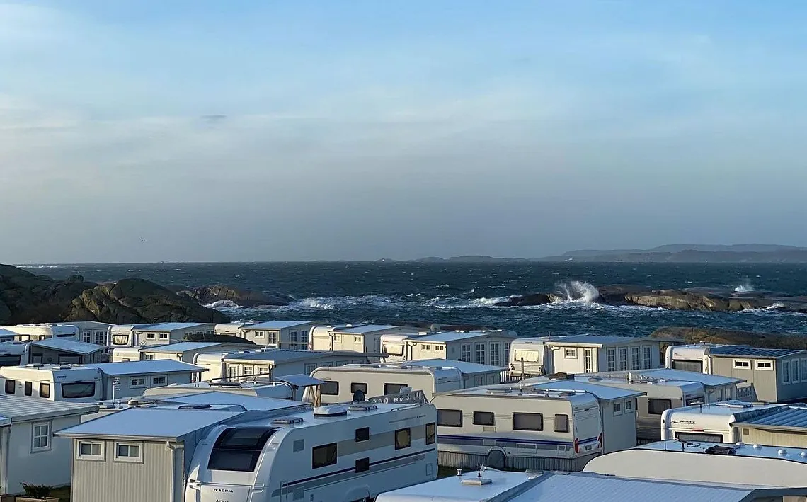 Campingplass med spikertelt, bobiler og campingvogner med havet i bakrunn.
